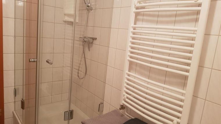 A modern bathroom with a shower stall and white tiles. Towels are neatly placed on a bench, and a towel warmer is mounted on the wall.