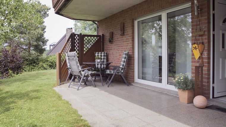 A cozy patio with garden furniture and a small table. In the background, grasses and trees can be seen.