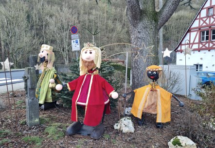 Drei Figuren der Heiligen Drei Könige in bunten Gewändern stehen vor einem Baum. Im Hintergrund sind ein Fachwerkhaus und ein Verkehrsschild zu sehen., © Svenja Schulze-Entrup