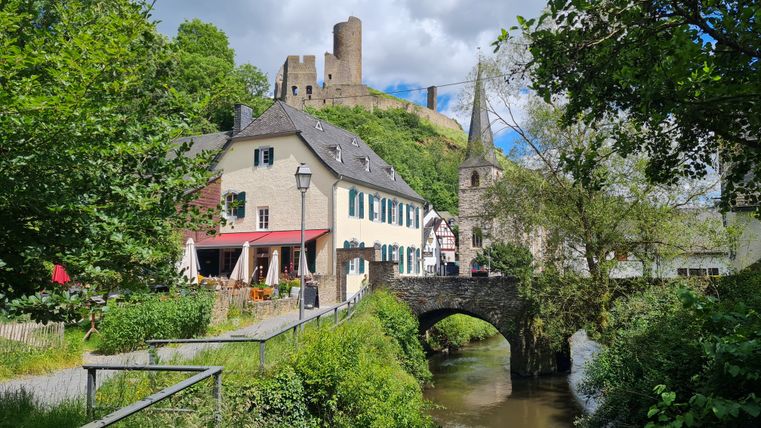 Burg und Kirche in Monreal, Deutschland, mit Fluss und Brücke im Vordergrund.