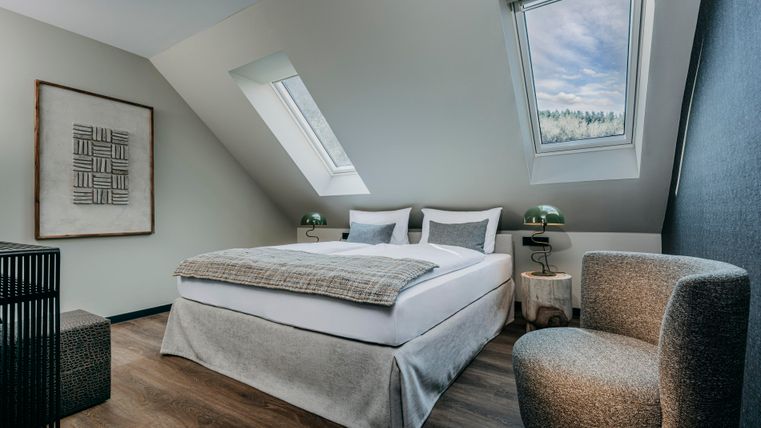 Ein modernes Schlafzimmer mit einem großen Bett und stilvoller Einrichtung. Große Fenster lassen viel Tageslicht herein und bieten eine schöne Aussicht.