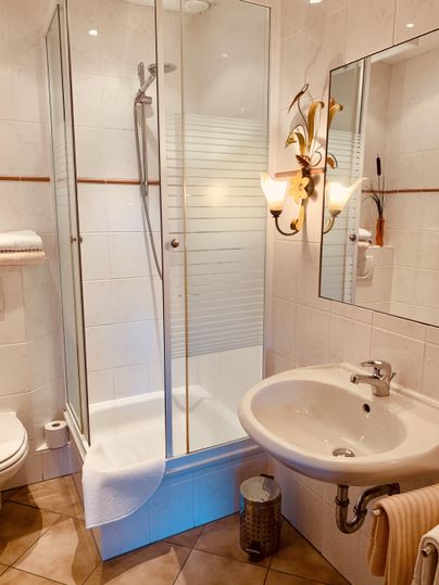 Ein modernes Badezimmer mit einer Duschkabine und einem Waschbecken. Die Wände sind hell gefliest und die Ausstattung ist sauber und funktional.