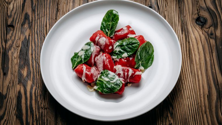 Ein Teller mit gefüllten Paprika, garniert mit frischem Spinat und einer cremigen Sauce. Der Kontrast zwischen den roten Paprika und den grünen Blättern wirkt ansprechend.