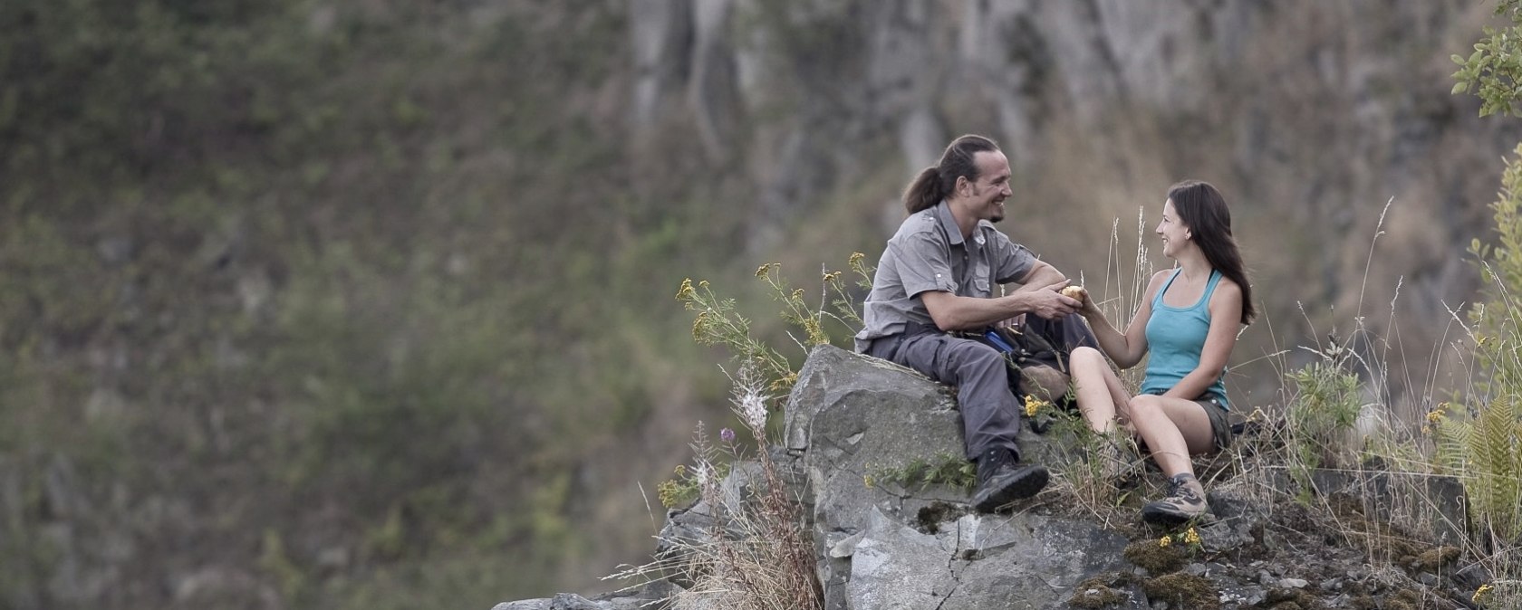 Zwei Personen sitzen auf einem Felsen im Steinbruch, umgeben von Pflanzen. Sie unterhalten sich und wirken entspannt., &copy; Traumpfade/Kappest