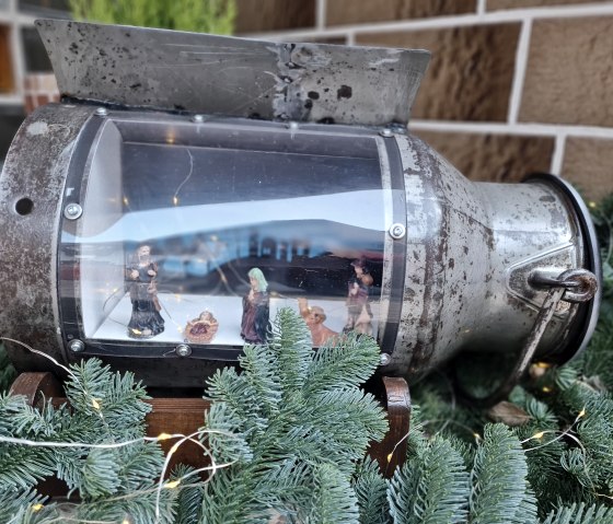 Weihnachtsszene in alter Milchkanne mit Krippenfiguren, umgeben von Tannenzweigen und Lichterkette., &copy; Svenja Schulze-Entrup