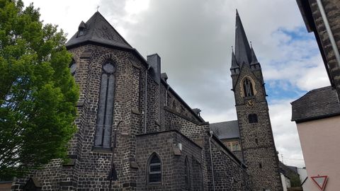 Eine alte Kirche mit einem hohen Turm und einem charakteristischen Steinfassaden. Der Himmel ist bewölkt und die Umgebung wirkt ruhig.