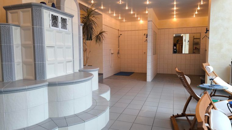 Ein heller Wellnessbereich mit einem großen Heizofen und modernen Sanitäreinrichtungen. Bequeme Stühle laden zum Entspannen ein.
