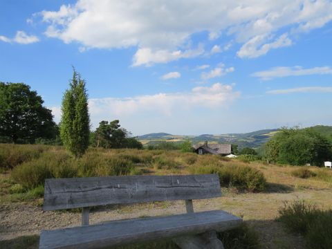 Eine wunderschöne Landschaft mit einem Blick auf Hügel und Bäume. Im Vordergrund steht eine Holzbank.