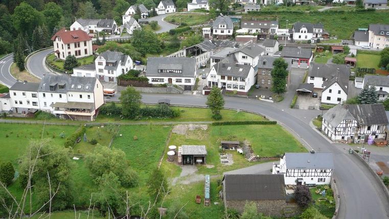 Eine malerische Landschaft mit kleinen Häusern und grünen Wiesen. Die Straße windet sich durch das Dorf und wird von Bäumen umgeben.
