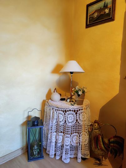 Eine gemütliche Ecke mit einem Tisch aus Spitze und einer Lampe. Neben dem Tisch stehen eine Laterne und ein dekorativer Hahn.