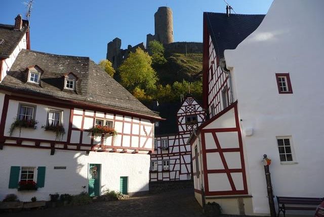 A picturesque old town with traditional half-timbered houses. In the background, a castle ruin can be seen on a hill.