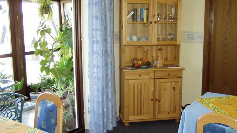 A cozy room with a wooden cupboard and plant elements. Two tables with yellow tablecloths are visible in the foreground.