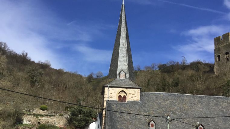 Eine Kirche mit einem spitzen Turm steht in einer hügeligen Landschaft. Die klare blaue Himmel sorgt für eine schöne Kulisse.