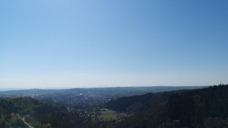 Ein schöner Ausblick über eine Stadt mit grünen Feldern und Wäldern im Hintergrund. Der Himmel ist klar und blau.