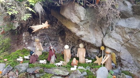 A wooden nativity scene under a rock, depicted with figures reenacting a scene from the Christmas story. Surrounded by moss and small animals.