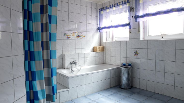 A modern bathroom with blue and white tiles. There is a bathtub, a shower curtain, and large windows that provide daylight.