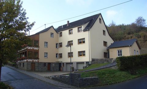A modern residential building with several floors and a mixed facade. The street is quiet, surrounded by trees and hills.