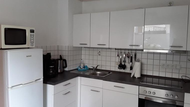 A modern kitchen with white cabinets and a stainless steel stove. There is a refrigerator and a microwave as well as various kitchen appliances.