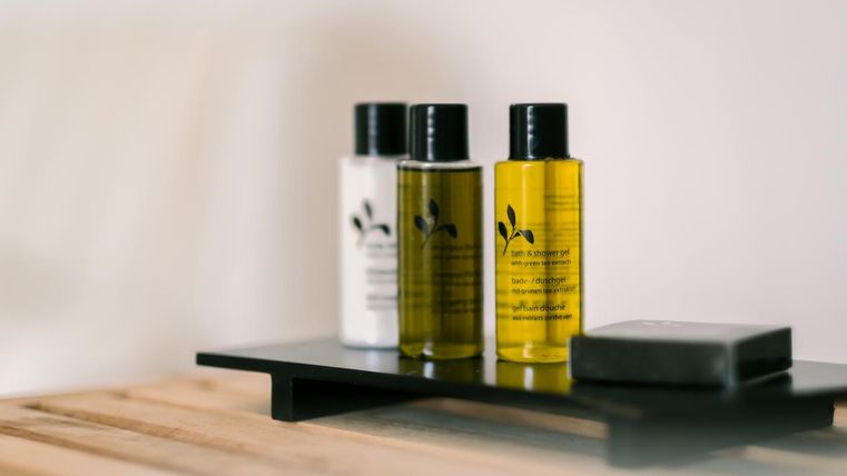 Three bottles of care products and a bar of soap are on a modern wooden tray. The bottles are in different colors and contain natural ingredients.