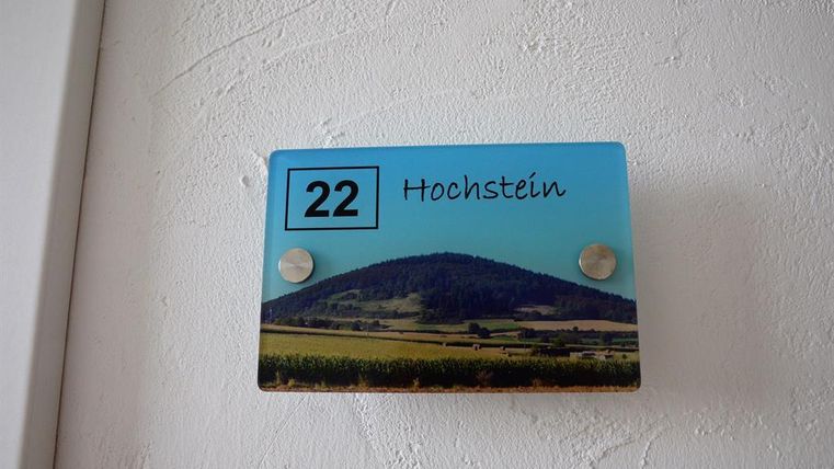 A nameplate with the number 22 and the word "Hochstein." In the background, a landscape featuring a hill and fields is depicted.