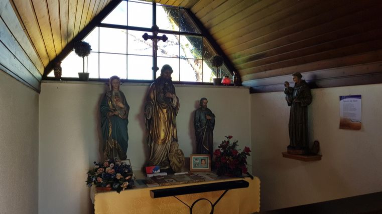 A small room with religious statues and ornate decoration. A window lets in natural light and creates a calm atmosphere.