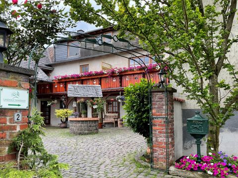 An inviting courtyard with a paved path and colorful flowers. In the background, there is a charming building with wooden details and a cozy seating area.