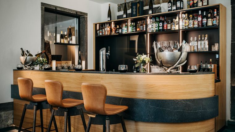 Eine elegante Bar mit Holz- und Steinelementen. Auf dem Regal sind verschiedene Spirituosen und Getränke sichtbar.