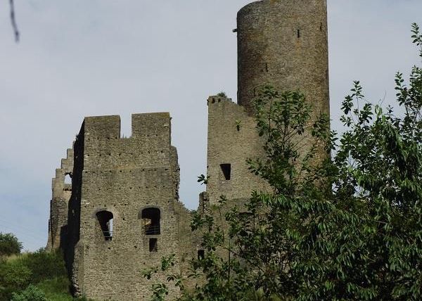 An old castle ruin surrounded by green trees. The sky is slightly cloudy, and the structure is partly collapsed.