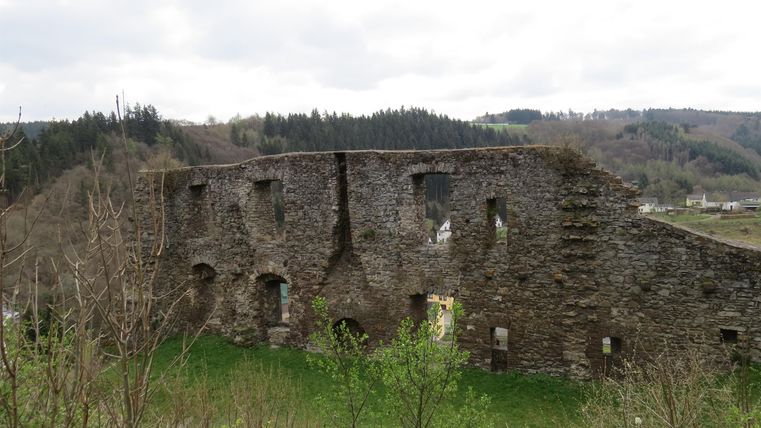An old ruin with stone walls, surrounded by green meadows and gentle hills. The sky is cloudy, giving the scene a mystical atmosphere.