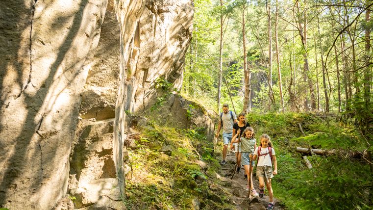 Family hiking on a forest path next to a rock face.