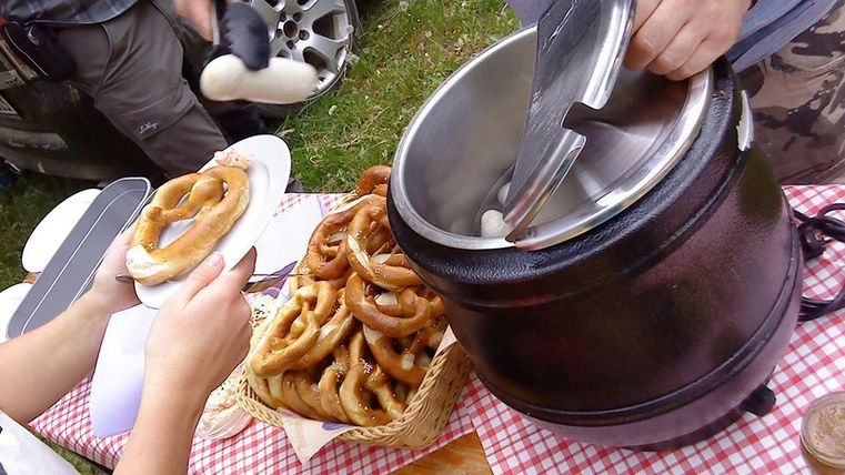 A stand with freshly baked pastries, including pretzels. People serve and enjoy the snacks outdoors.
