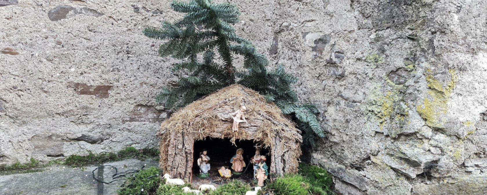 Eine kleine Krippe mit Figuren und Moos steht vor einer alten Steinmauer. Ein Tannenzweig ziert das Dach., © Svenja Schulze-Entrup