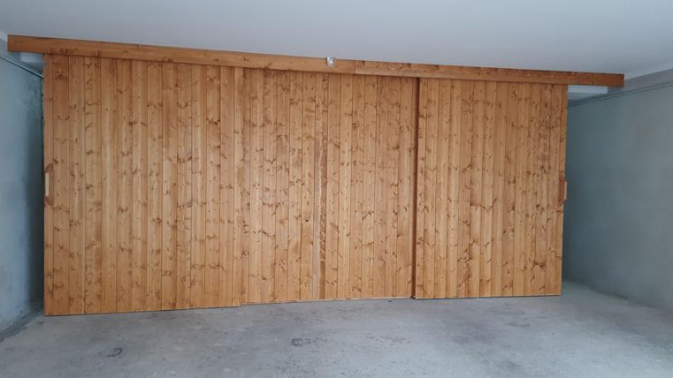 A wooden sliding door in a garage. The room is simple and has a gray concrete floor.