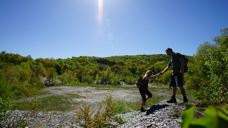 Two people hiking in a green landscape under a bright blue sky.