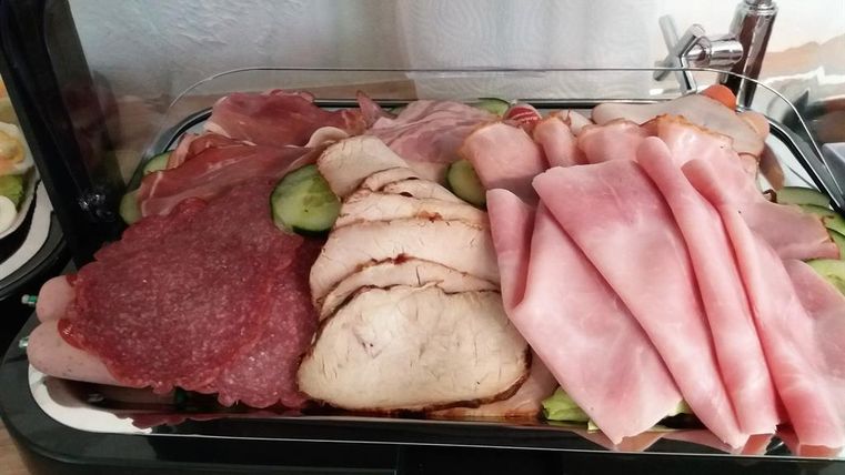 A selection of various sausages and meats, beautifully arranged on a plate. There are also some cucumber slices visible.
