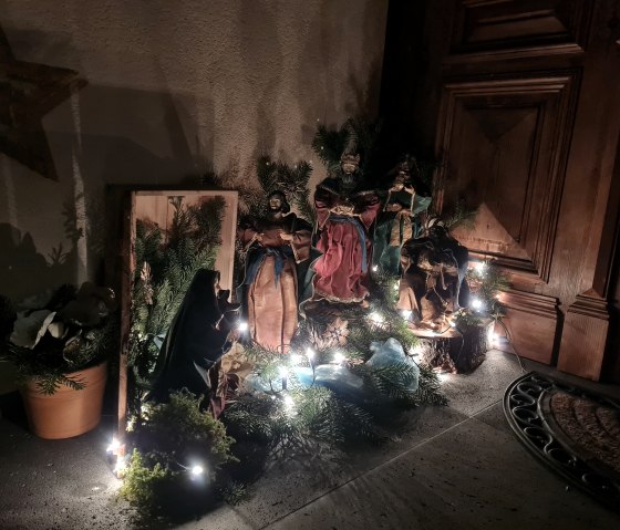 Weihnachtliche Krippenszene mit Figuren, Tannenzweigen und Lichterkette vor einer Holzt&uuml;r. Ein Stern h&auml;ngt an der Wand., &copy; Svenja Schulze- Entrup