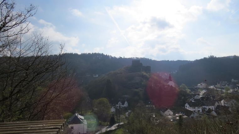 A landscape with gentle hills and a clear sky. In the foreground, there are trees and a view of a small village.
